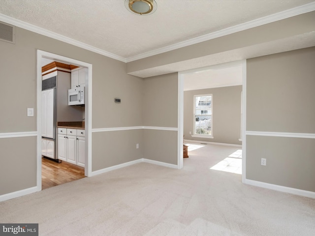 empty room with crown molding, baseboards, visible vents, and light colored carpet