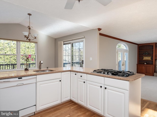 kitchen featuring stainless steel gas stovetop, light wood-style flooring, vaulted ceiling, white dishwasher, and a sink