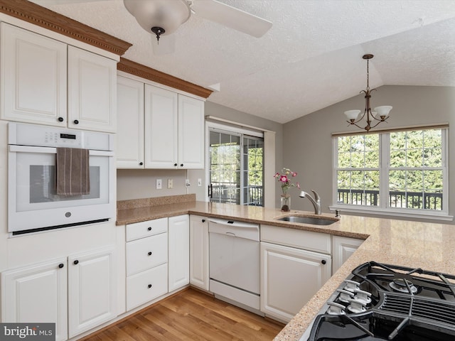 kitchen featuring decorative light fixtures, light wood-style floors, white cabinetry, a sink, and white appliances