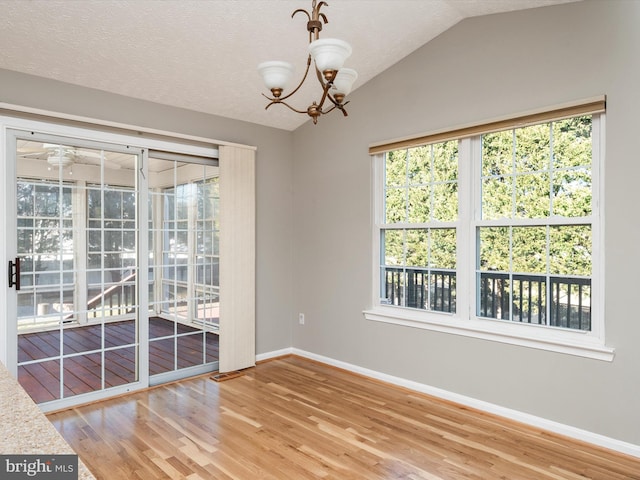 empty room featuring a wealth of natural light, lofted ceiling, baseboards, and light wood finished floors