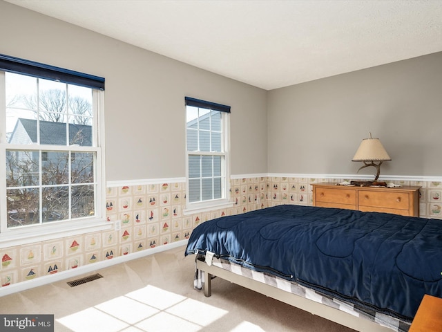 carpeted bedroom with a wainscoted wall, baseboards, visible vents, and wallpapered walls