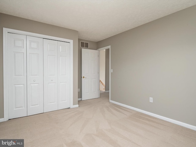 unfurnished bedroom featuring carpet, a closet, visible vents, a textured ceiling, and baseboards