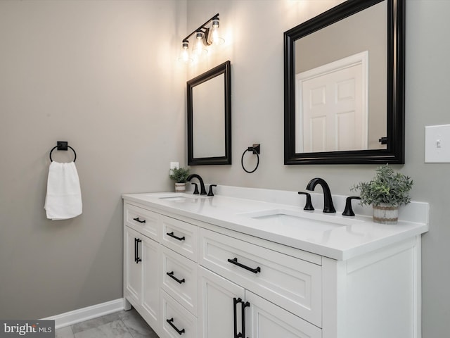 bathroom with marble finish floor, double vanity, a sink, and baseboards