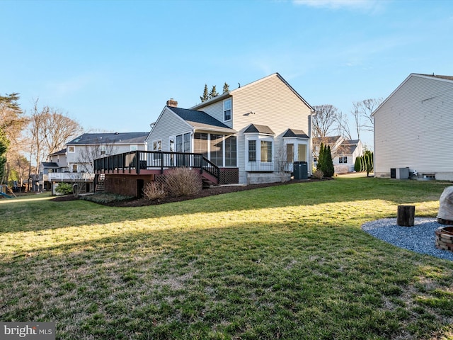 rear view of house featuring a chimney, a sunroom, a lawn, and a deck