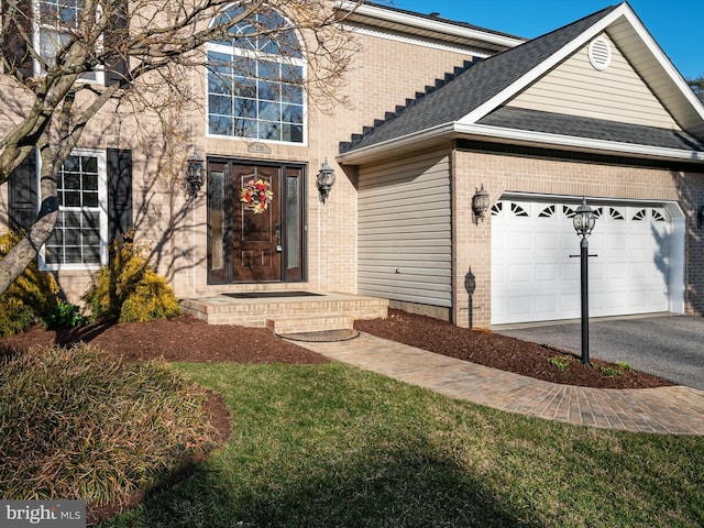 traditional-style house with a garage, brick siding, a shingled roof, aphalt driveway, and a front yard