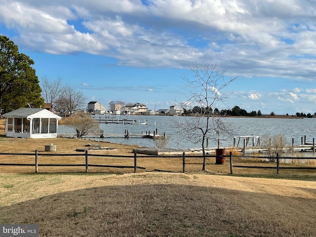 view of yard featuring a sunroom, fence, a dock, and a water view