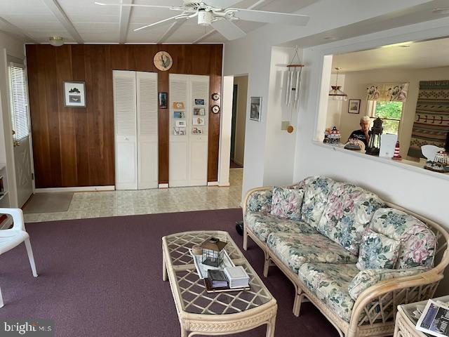 carpeted living room with wooden walls and ceiling fan