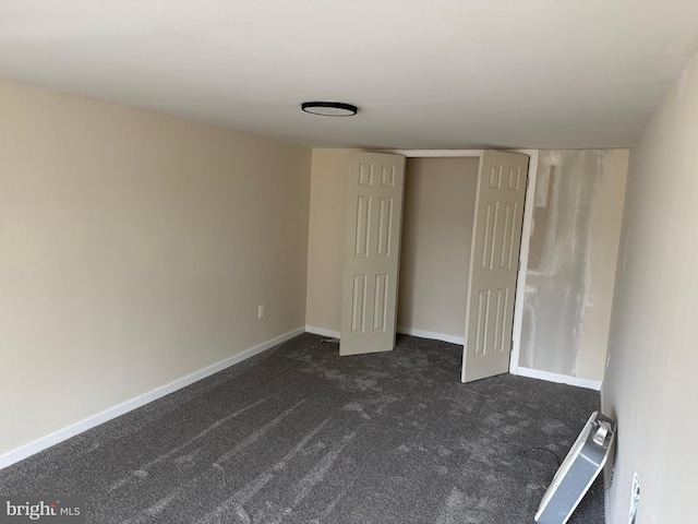 unfurnished room with baseboards and dark carpet