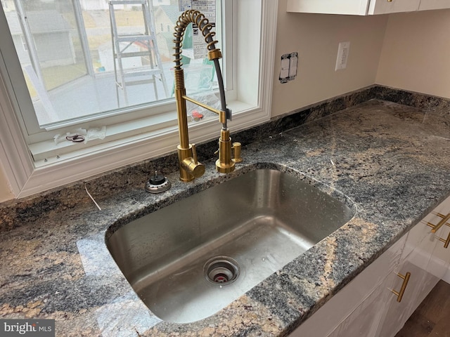 details with dark stone countertops, white cabinetry, and a sink