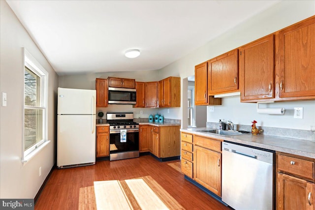 kitchen with stainless steel appliances, brown cabinetry, a sink, and wood finished floors