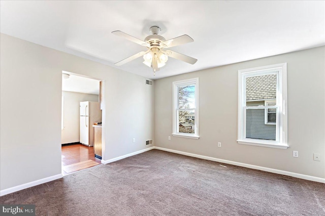 carpeted spare room featuring ceiling fan, visible vents, and baseboards