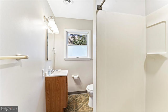 bathroom featuring toilet, vanity, visible vents, baseboards, and walk in shower