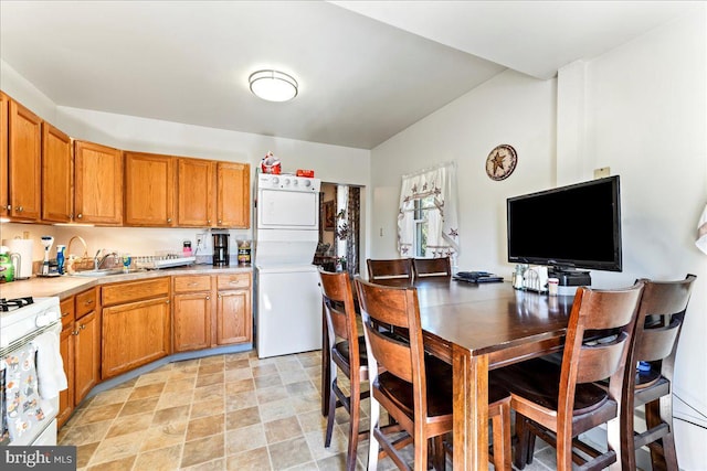 kitchen featuring brown cabinetry, white range with gas cooktop, light countertops, and stacked washer and clothes dryer