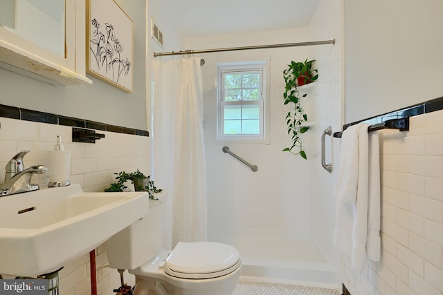bathroom with a shower stall, tile walls, toilet, a sink, and a wainscoted wall