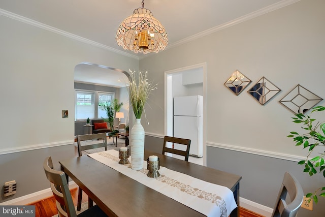 dining space with arched walkways, a chandelier, crown molding, baseboards, and wood finished floors