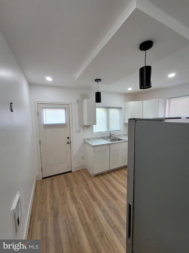 kitchen with light wood-style floors, white cabinets, light countertops, freestanding refrigerator, and decorative light fixtures