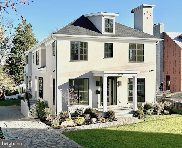 view of front of home with a shingled roof, a chimney, a front yard, and stucco siding