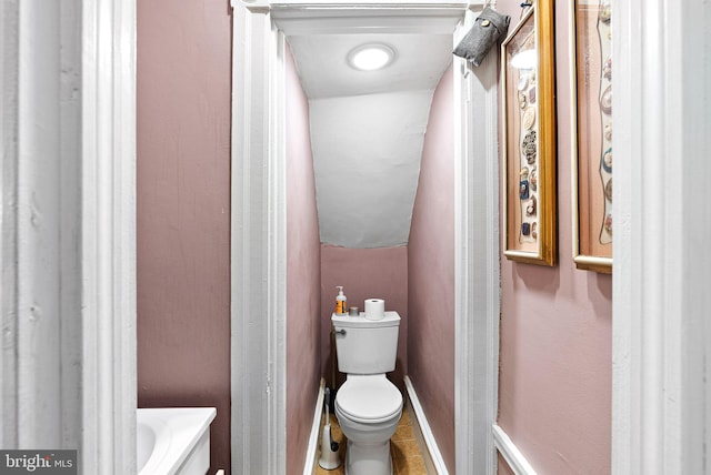 bathroom with baseboards, vaulted ceiling, toilet, and tile patterned flooring