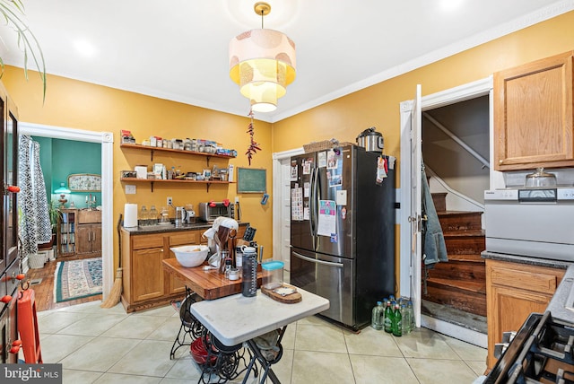 kitchen with light tile patterned flooring, dark countertops, crown molding, and freestanding refrigerator