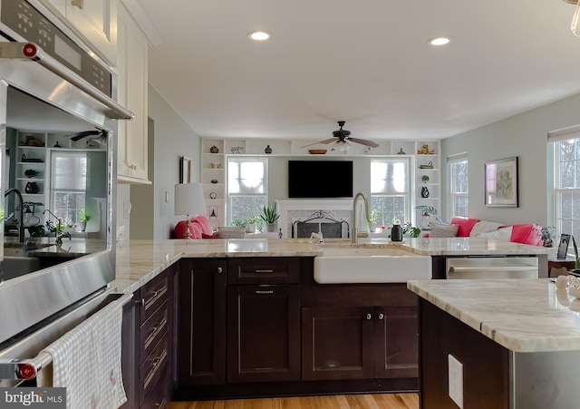 kitchen with a sink, light stone counters, open floor plan, stainless steel appliances, and a fireplace