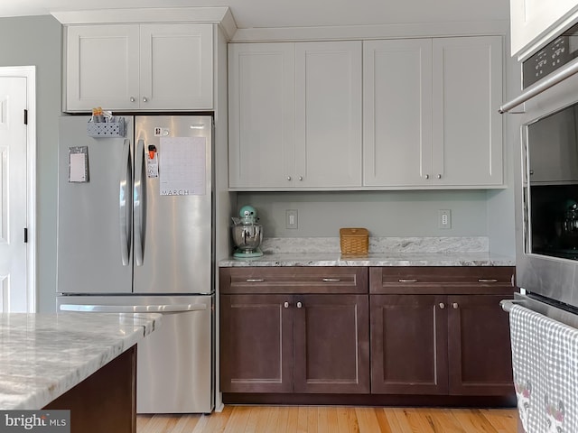 kitchen with light wood-style flooring, appliances with stainless steel finishes, white cabinets, light stone countertops, and dark brown cabinets