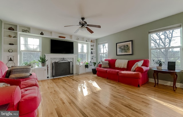 living room with plenty of natural light, built in shelves, a fireplace with flush hearth, and light wood finished floors