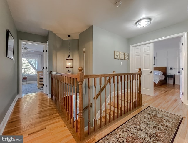 hall with an upstairs landing, baseboards, and light wood finished floors