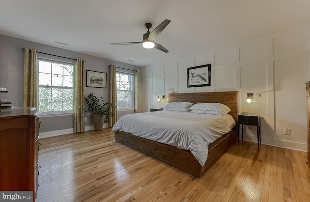 bedroom featuring visible vents, baseboards, light wood-type flooring, a decorative wall, and a ceiling fan