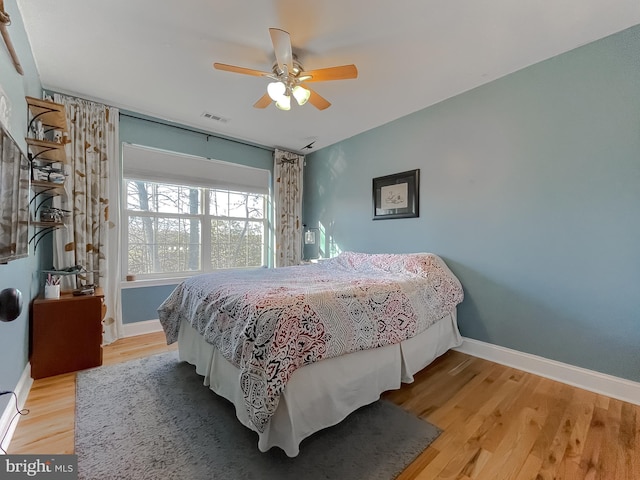 bedroom featuring ceiling fan, visible vents, baseboards, and wood finished floors