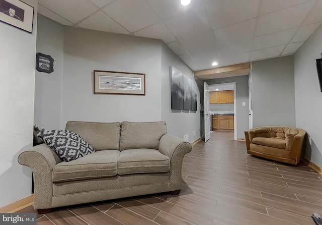 living area featuring a drop ceiling, baseboards, and wood finish floors