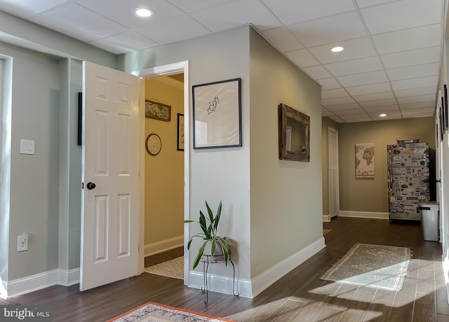 hall with dark wood finished floors, a paneled ceiling, and baseboards