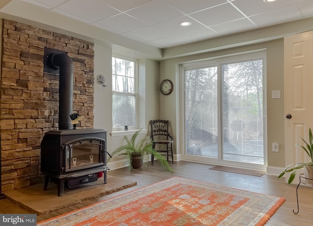 sitting room with a wood stove, wood finished floors, baseboards, and a drop ceiling