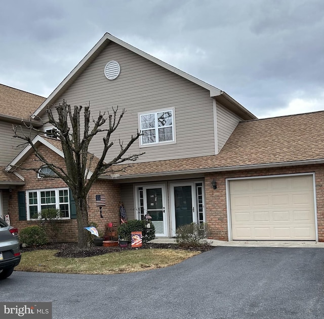 traditional-style home featuring an attached garage, roof with shingles, aphalt driveway, and brick siding