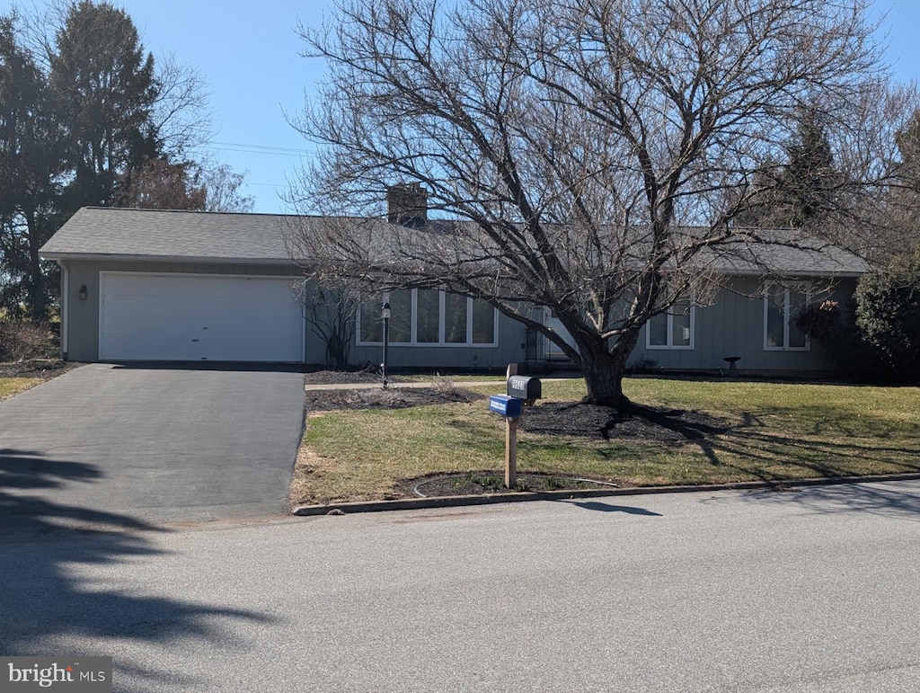 view of front facade with aphalt driveway, a front lawn, a chimney, and an attached garage