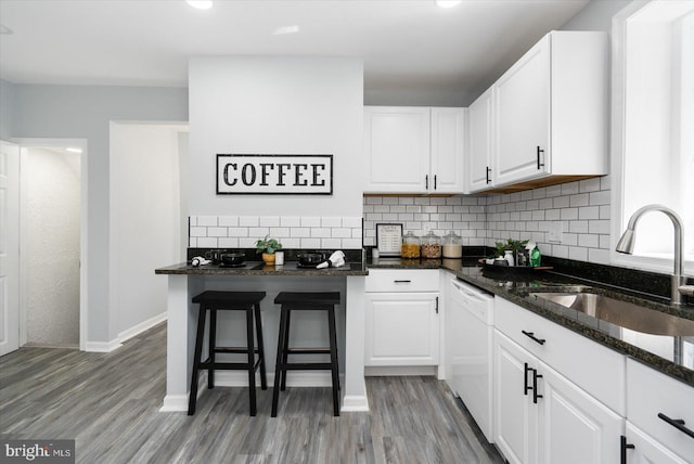 kitchen featuring a sink, white cabinetry, dark stone counters, decorative backsplash, and dishwasher