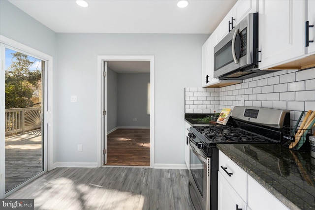 kitchen featuring wood finished floors, baseboards, white cabinets, appliances with stainless steel finishes, and tasteful backsplash