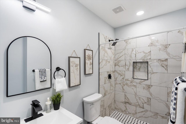 bathroom featuring a sink, visible vents, tiled shower, and toilet