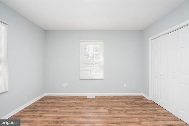 unfurnished bedroom featuring a closet, baseboards, visible vents, and wood finished floors