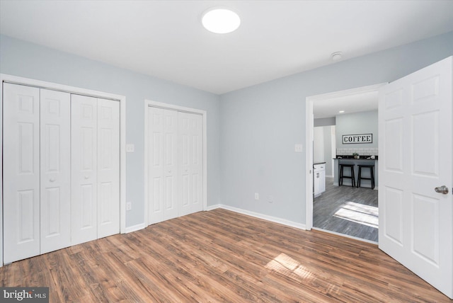 unfurnished bedroom with baseboards, two closets, and wood finished floors