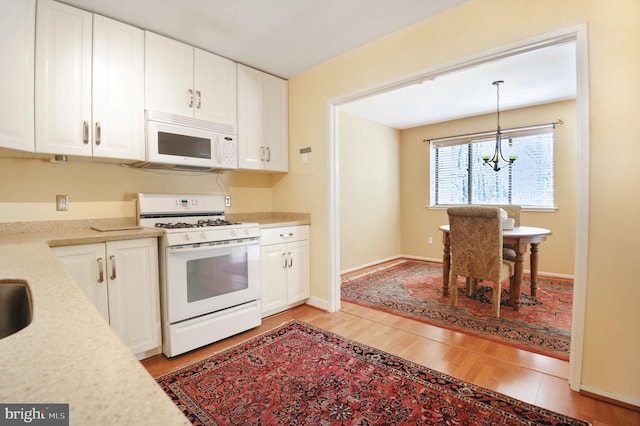 kitchen with light wood finished floors, white appliances, an inviting chandelier, and white cabinetry