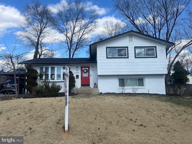 tri-level home with brick siding, a front yard, and fence