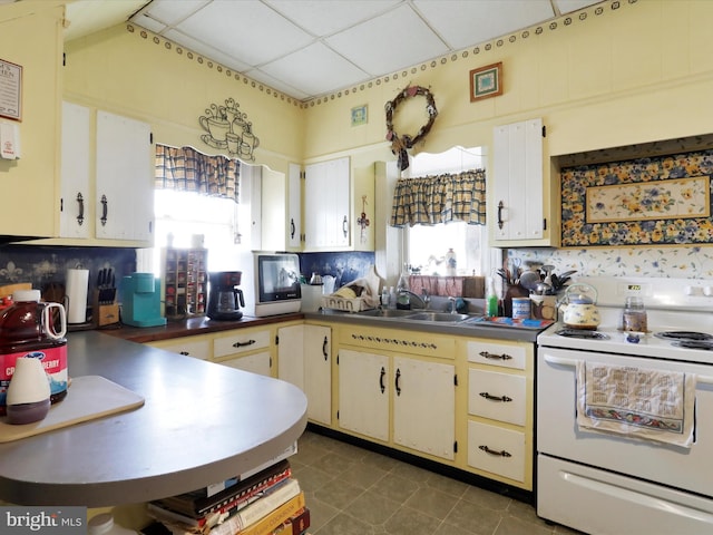 kitchen featuring cream cabinetry, a paneled ceiling, electric range, a sink, and tile patterned flooring