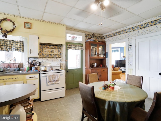 kitchen featuring a drop ceiling, a sink, electric stove, glass insert cabinets, and wallpapered walls