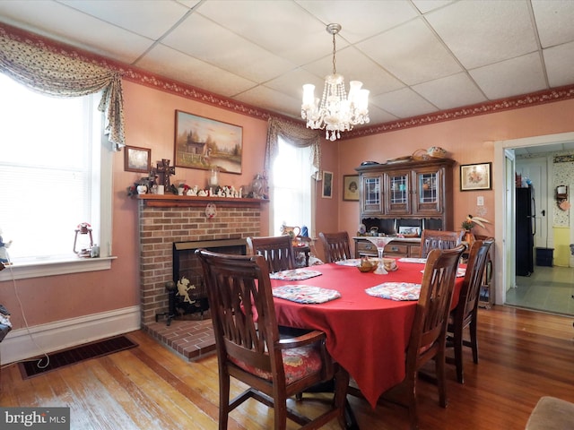 dining area with a drop ceiling, wood finished floors, visible vents, and a brick fireplace