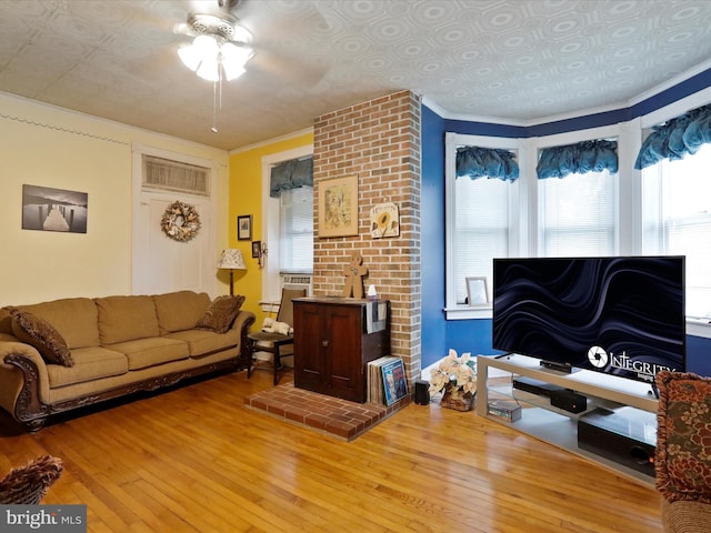 living room with a ceiling fan, hardwood / wood-style flooring, an ornate ceiling, ornamental molding, and a wood stove