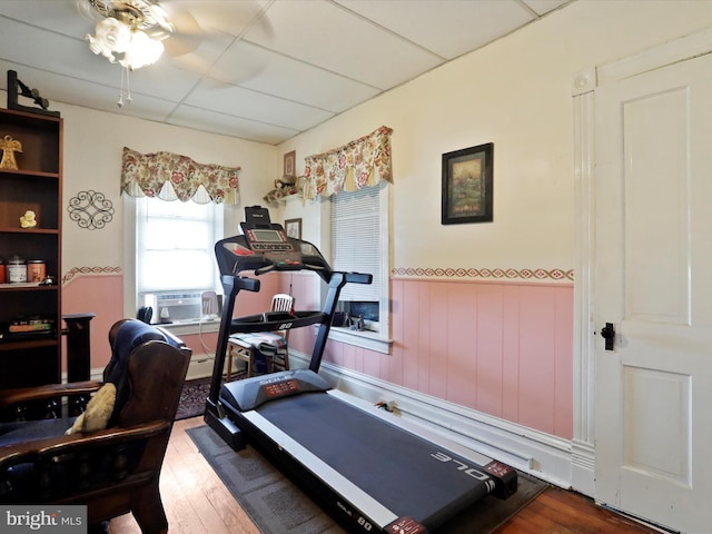 exercise area featuring a ceiling fan, wainscoting, wood finished floors, cooling unit, and a paneled ceiling