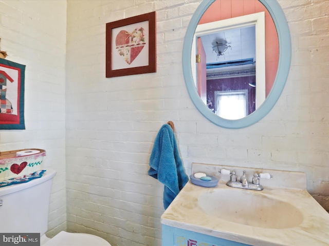 bathroom featuring toilet, brick wall, and vanity