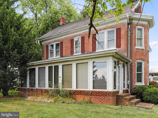 view of home's exterior featuring a sunroom, a chimney, and brick siding