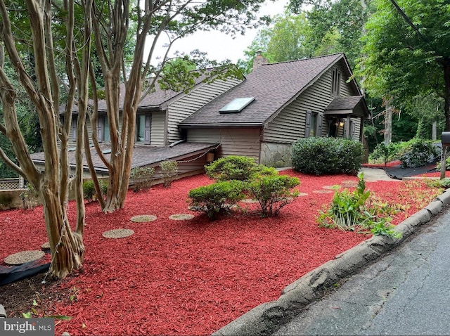 view of front of property featuring roof with shingles, a chimney, and a wooden deck