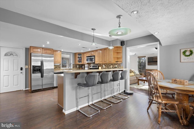 kitchen with dark wood finished floors, open shelves, stainless steel appliances, a peninsula, and a kitchen bar